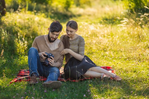young couple sits in nature and looks at the camera at the resulting picture