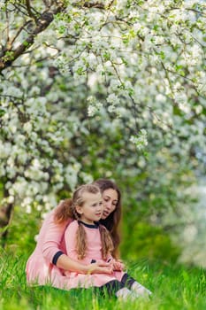 mother and daughter walk through a blooming apple orchard