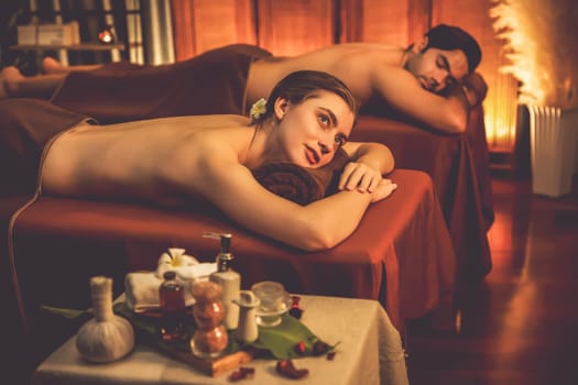 Caucasian couple customer enjoying relaxing anti-stress spa massage and pampering with beauty skin recreation leisure in warm candle lighting ambient salon spa at luxury resort or hotel. Quiescent