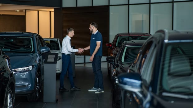 Seller and buyer shake hands in a car dealership. Caucasian man buys a car