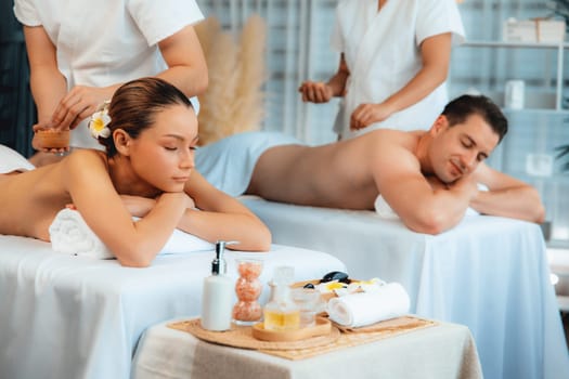 Blissful couple customer having exfoliation treatment in luxury spa salon with warmth candle light ambient. Salt scrub beauty treatment in health spa body scrub. Quiescent