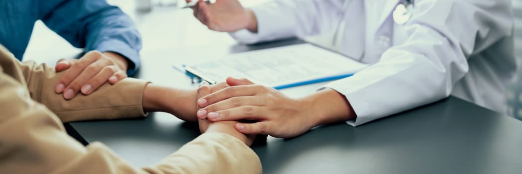 Doctor providing compassionate healthcare consultation while young couple patient holding hand, comfort each other after infertile report. Reproductive and medical fertility consulting. Neoteric