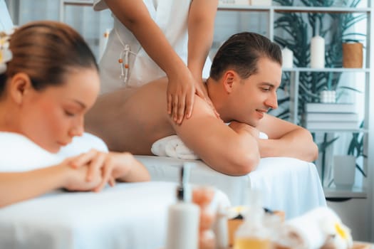 Caucasian couple customer enjoying relaxing anti-stress spa massage and pampering with beauty skin recreation leisure in day light ambient salon spa at luxury resort or hotel. Quiescent