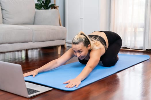 Senior woman in sportswear being doing yoga in meditation posture on exercising mat at home. Healthy senior pensioner lifestyle with peaceful mind and serenity. Clout