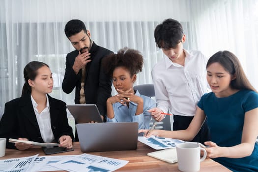 Multiracial analyst team use BI dashboard data to analyze financial report on meeting table. Group of diverse business people utilize data analysis by FIntech for success business marketing. Concord