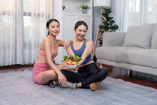 Young sporty Asian women in sportswear holding salad bowl together fill with vibrant of fruit and vegetable. Natural youthful and fit body lifestyle with balance nutrition and home exercise. Vigorous