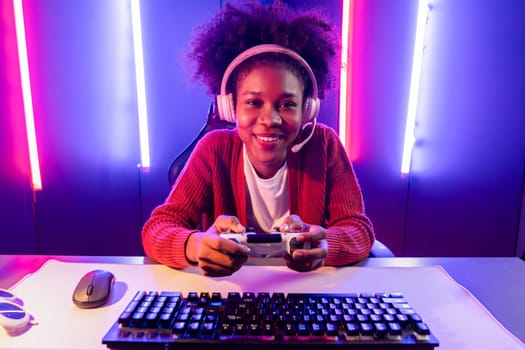 Host channel of gaming streamer, African girl playing online game with joystick, talking with viewers media online on microphone. Esport skilled team players in neon color lighting room. Tastemaker.