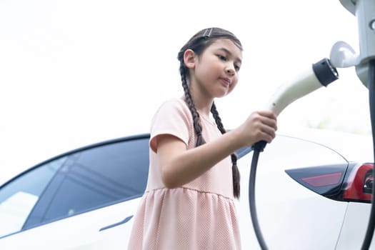 Little young girl learn about eco-friendly and energy sustainability as she recharge electric vehicle from EV charging station. EV car and sustainable future generation concept. Synchronos