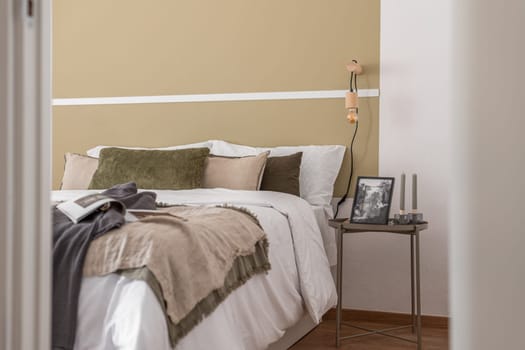 Side shot of edge of large cozy double bed with a bedside table in beige color in a hotel room. The concept of comfortable living in a business hotel with a convenient location and five-star service.