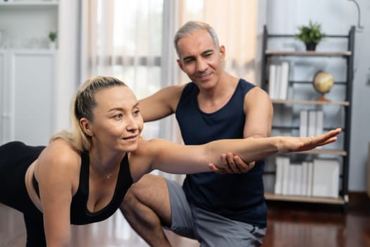 Happy active senior couple in sportswear being supportive and assist on yoga posture together at home. Healthy senior man and woman lifestyle with yoga exercise. Clout