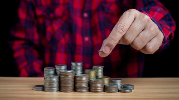 Human puts money on pile of coins. Ideas for investing and growing a business, maximizing profits from business, ideas for setting savings goals and setting goals for fixed deposits with banks.