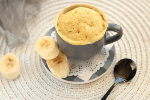 cupcake in a mug with banana pieces. Banana cupcake on a light background. vanilla biscuit in a mug. The concept of a dessert in the microwave. bananas cake. High quality photo