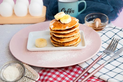 breakfast, ingredients, recipe. homemade banana pancakes with honey. Pancakes on kitchen table against the background of eggs and cups with coffee. Pancake slide with honey topping and fresh bananas