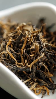 A closeup of dried tea leaves showcasing their unique texture and color variations, presented elegantly in a dish