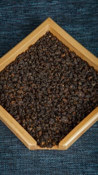 A closeup view of dark organic seeds delicately arranged in a rustic wooden tray placed on a textured surface