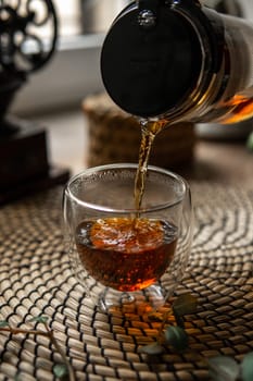 A warm, comforting cup of aromatic tea is being poured elegantly from a stylish pot into a clear glass cup
