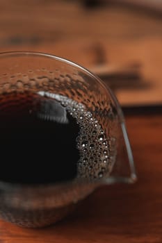 This image shows a closeup of a glass container filled with a rich dark liquid with bubbles on the surface