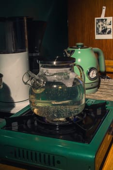 A beautiful glass teapot gently boils water on a charming green stove, creating a warm and inviting kitchen atmosphere