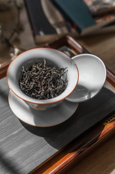A visually appealing display of delicate dried tea leaves in a porcelain cup on a charming wooden tray