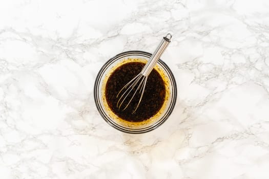 A top-down view of the wet ingredients in a bowl, including dark molasses, eggs, and fresh orange zest, ready to be whisked together for the Zesty Orange Gingerbread Cookie Dough recipe. A small whisk rests in the bowl, emphasizing the recipe citrusy, zesty twist.
