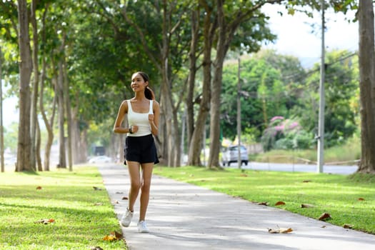 Full length of happy sportswoman running through a scenic park trail.