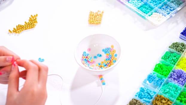 Delicate fingers of a young girl navigate through a treasure trove of bright, multicolored beads, each compartment revealing a new hue to choose from. Shes immersed in the joyful task of stringing together a handmade bracelet, with golden beads and pearls lying nearby to add a touch of sparkle to her creation.