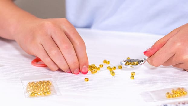 Delicate fingers of a young girl navigate through a treasure trove of bright, multicolored beads, each compartment revealing a new hue to choose from. Shes immersed in the joyful task of stringing together a handmade bracelet, with golden beads and pearls lying nearby to add a touch of sparkle to her creation.