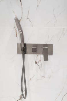 Luxury chrome faucet and shower in shower stall with white marble walls. Modern luxury shower cubicle.