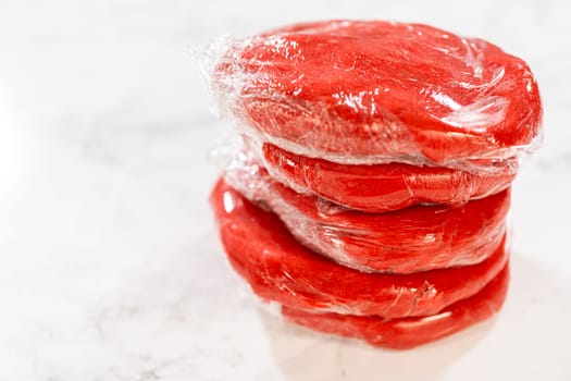 Four portions of the Classic Red Gingerbread Dough, each wrapped in plastic, are stacked and ready for refrigeration. This step allows the dough to rest and develop flavor before baking.