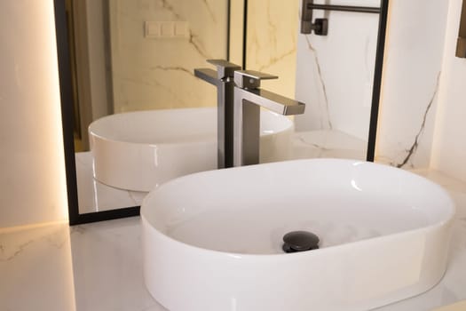 Chrome water faucet and white pedestal sink in bathroom . Stylish bathroom.