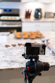 A DSLR camera, set up in a sleek, modern kitchen, captures the making of a video recipe for vlogging.