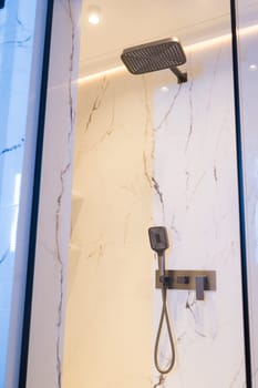 Luxury chrome faucet and shower in shower stall with white marble walls. Modern luxury shower cubicle.