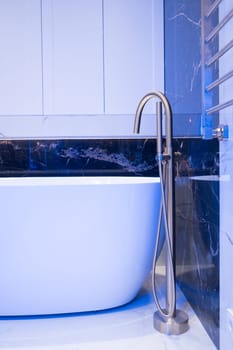 Modern bathroom interior. Exclusive stylish golden faucet on the floor near white bathtub on the background of granite wall.