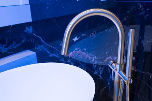 Closeup of silver bathroom faucet in bathroom next to white tub. Chrome faucet against a black granite wall.