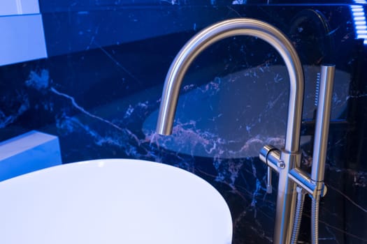Closeup of silver bathroom faucet in bathroom next to white tub. Chrome faucet against a black granite wall.