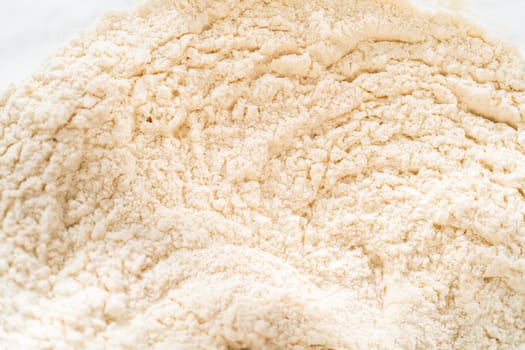Close-up view of dry ingredients for Classic Sugar Cookie Dough, including flour and sugar, showing a textured mix in a bowl. This macro shot captures the fine details of the flour's texture, essential for the cookie dough preparation process.