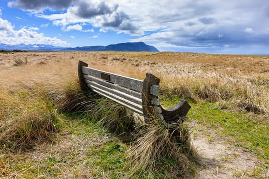 A park bench under a partly cloudy sky on Del Ray beach in Seaside, Oregon.