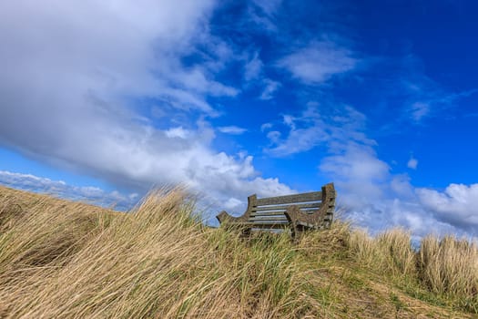 A park bench under a partly cloudy sky on Del Ray beach in Seaside, Oregon.