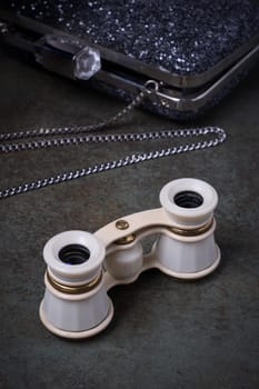 Vintage opera glasses with a black clutch are elegantly displayed. Image evokes nostalgia and luxury