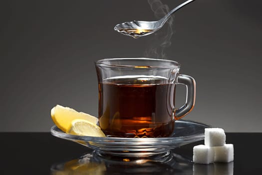 A close up image of a cup of hot tea with a spoon, lemon wedges, and sugar cubes.