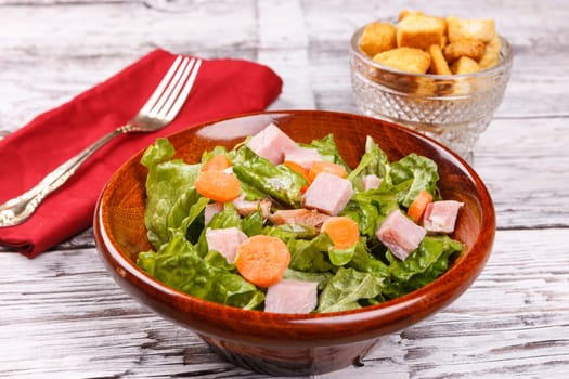 A close up of a salad with bits of ham and carrots.