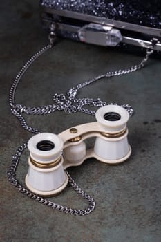 Vintage opera glasses with a black clutch are elegantly displayed. Image evokes nostalgia and luxury