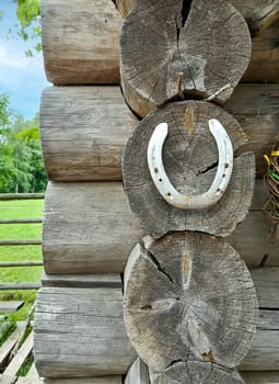 The corner of an old wooden log house is decorated with a metal horseshoe symbolizing protection and good luck.
