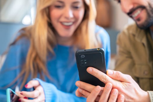A close-up view of a couple sharing a joyful moment. The man holds a smartphone as the woman smiles in the background, creating a warm and engaging atmosphere.