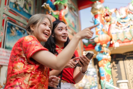 Two women enjoy the vibrant atmosphere of Chinese New Year celebrations pointing at colorful shrine decorations.