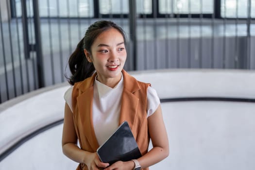 A confident businesswoman walks up stairs in a modern office, holding a tablet, exuding professionalism and determination.