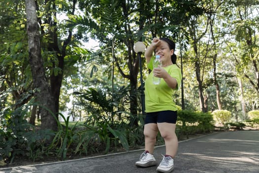 A petite woman jogs through a vibrant park, enjoying a sunny day while staying fit and hydrated.