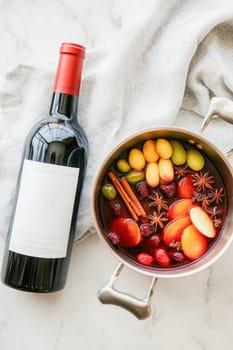 Pot with delicious mulled wine simmering with various fruits and spices, next to a bottle of red wine, perfect for christmas and winter holidays