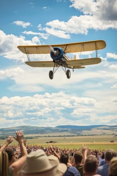 Spectators cheering a vintage yellow biplane flying over them at an air show
