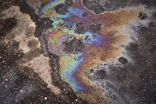 Colorful gasoline or oil spill creates rainbow sheen polluting cracked asphalt surface